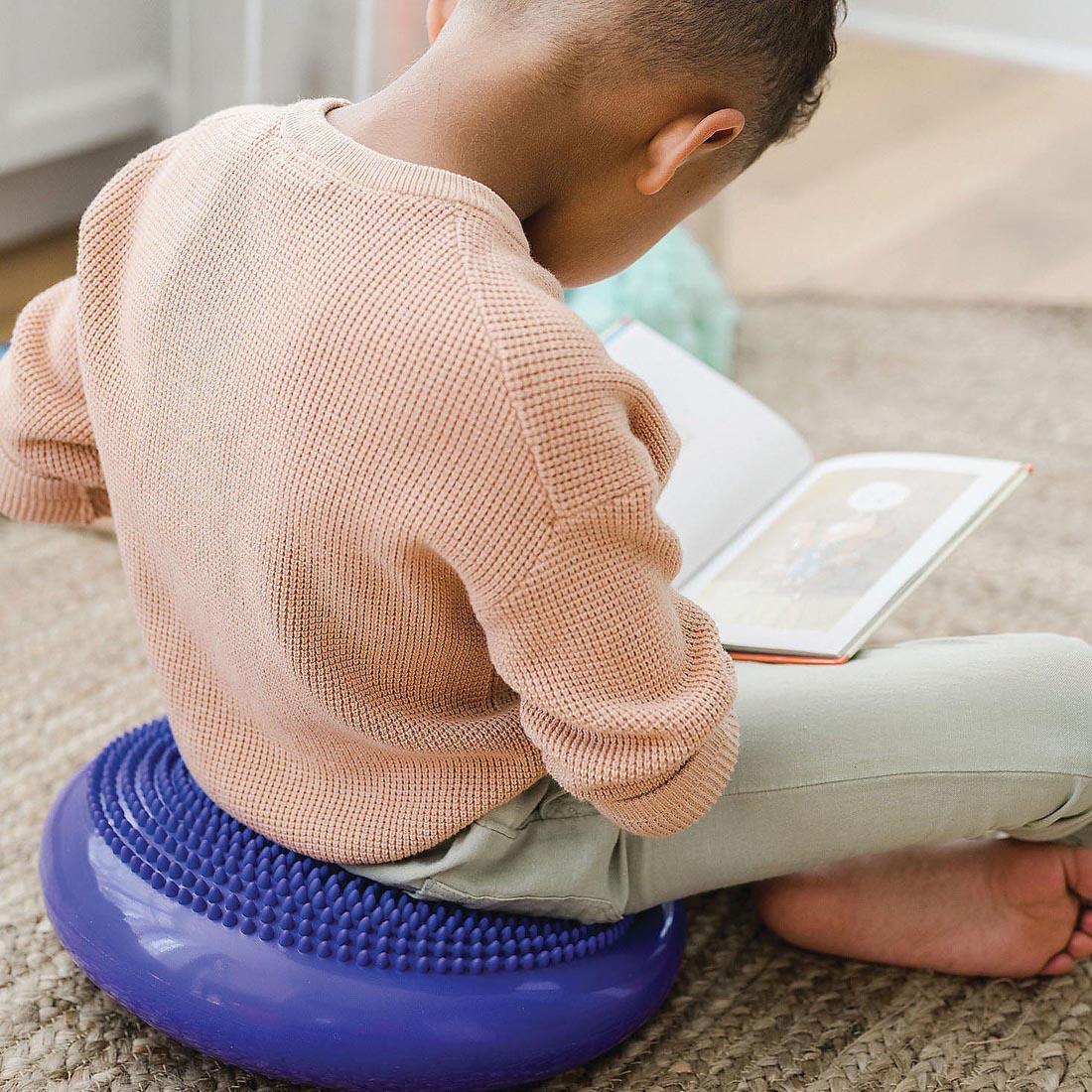 child sitting on the Sensory Genius Wobble Cushion By Mindware while reading