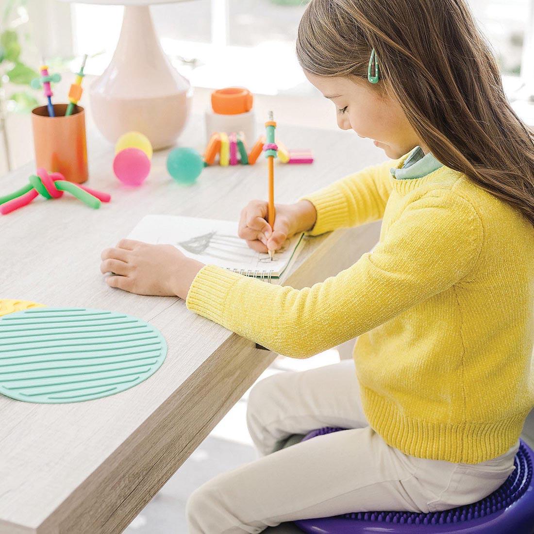 child sitting on the Sensory Genius Wobble Cushion By Mindware while working at a table