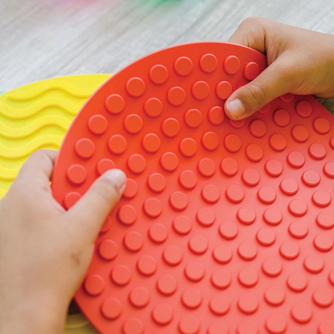 two small hands holding a Sensory Genius Sensory Mat By Mindware
