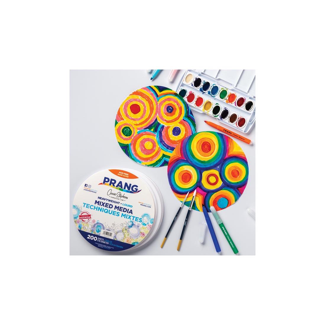 stack of Prang Mixed Media Paper Circles plus two painted ones shown with watercolor paints, brushes and markers