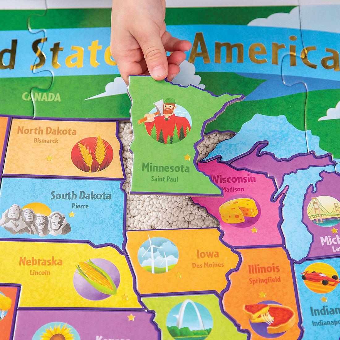child's hand placing a piece into the 54-Piece USA Floor Puzzle By Peaceable Kingdom