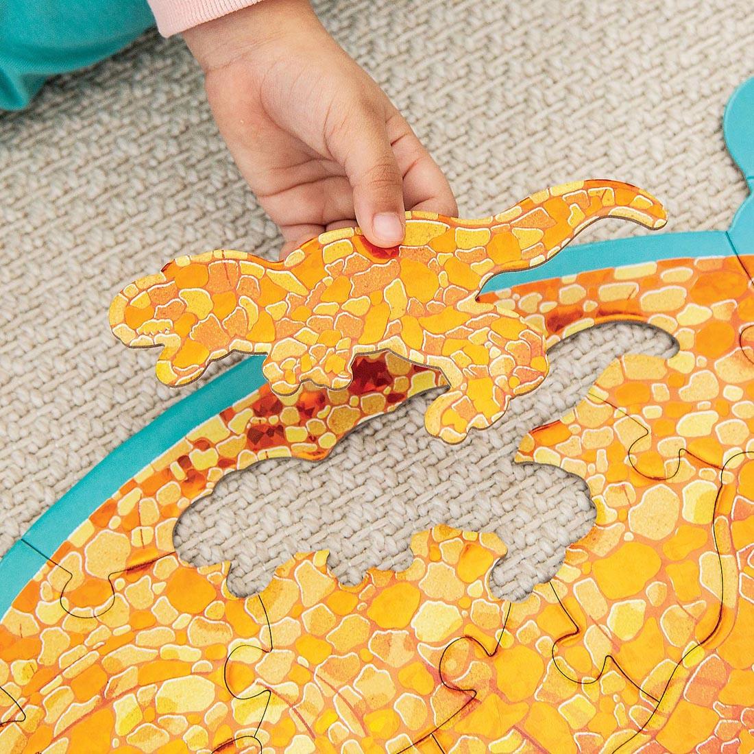 hand holding a t-rex-shaped puzzle piece from the Triceratops Floor Puzzle By Peaceable Kingdom