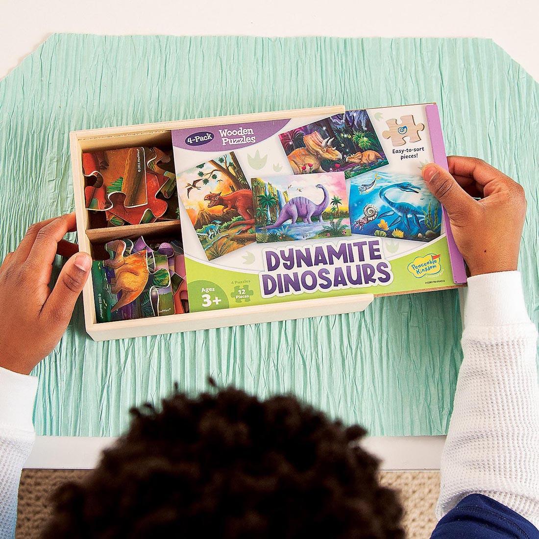 hands sliding open the package of Dynamite Dinosaurs Wooden Puzzles 4-Pack By Peaceable Kingdom