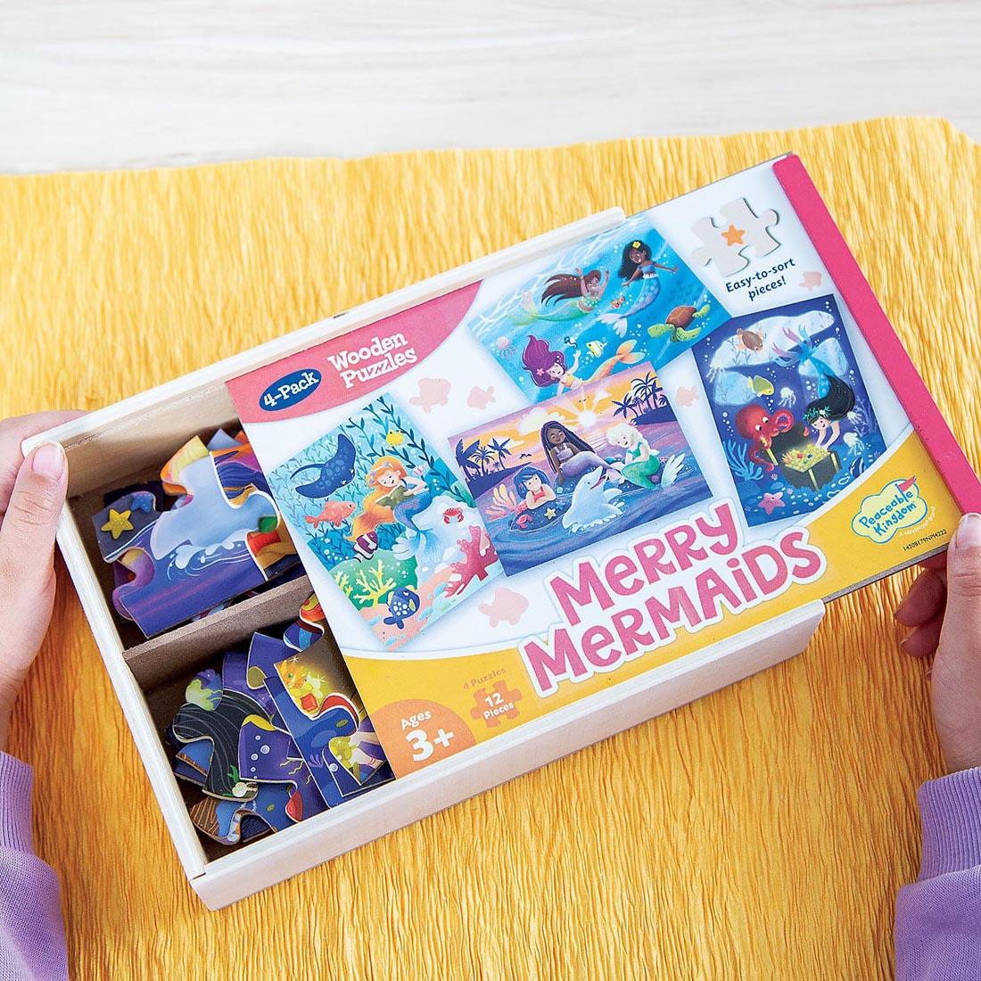 hands sliding open the package of Merry Mermaids Wooden Puzzles 4-Pack By Peaceable Kingdom