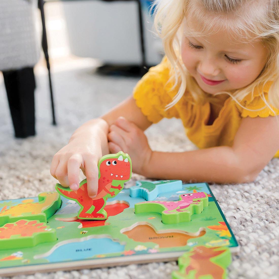 child lying on the floor playing with the My First Wooden Puzzle: Dinosaurs By Peaceable Kingdom