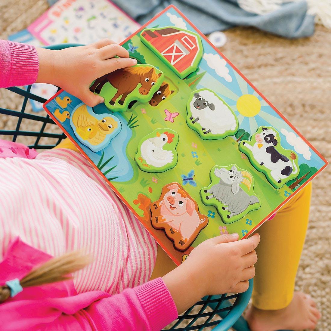 child playing with the My First Wooden Puzzle: Farm Animals By Peaceable Kingdom in their lap