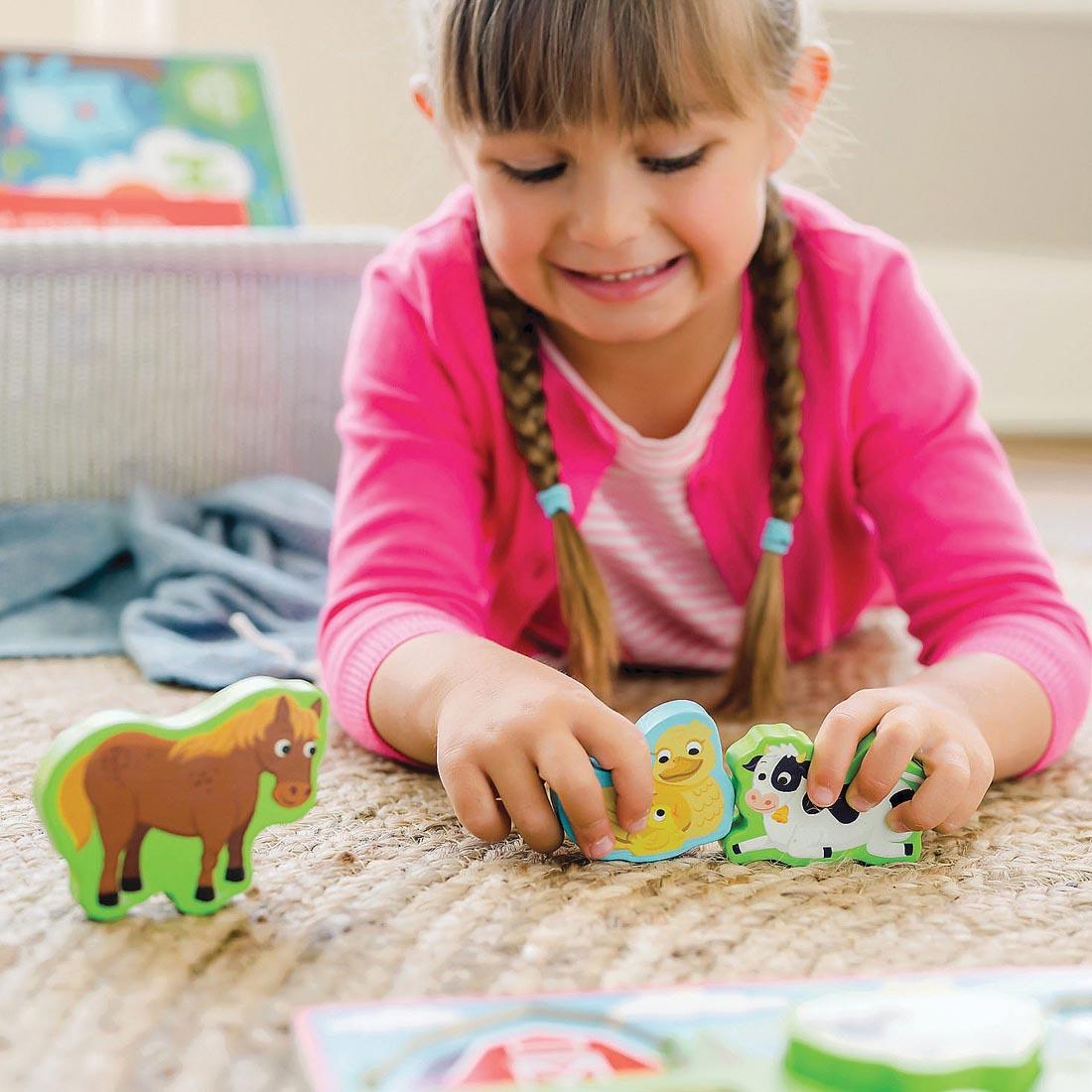 child lying on the floor playing with the animal pieces from My First Wooden Puzzle: Farm Animals By Peaceable Kingdom