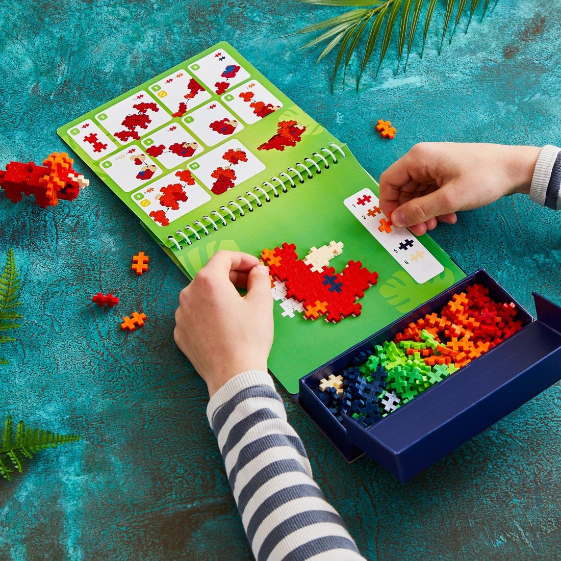 child's hands playing with the Plus-Plus Puzzle By Number Dinosaur Activity Pad