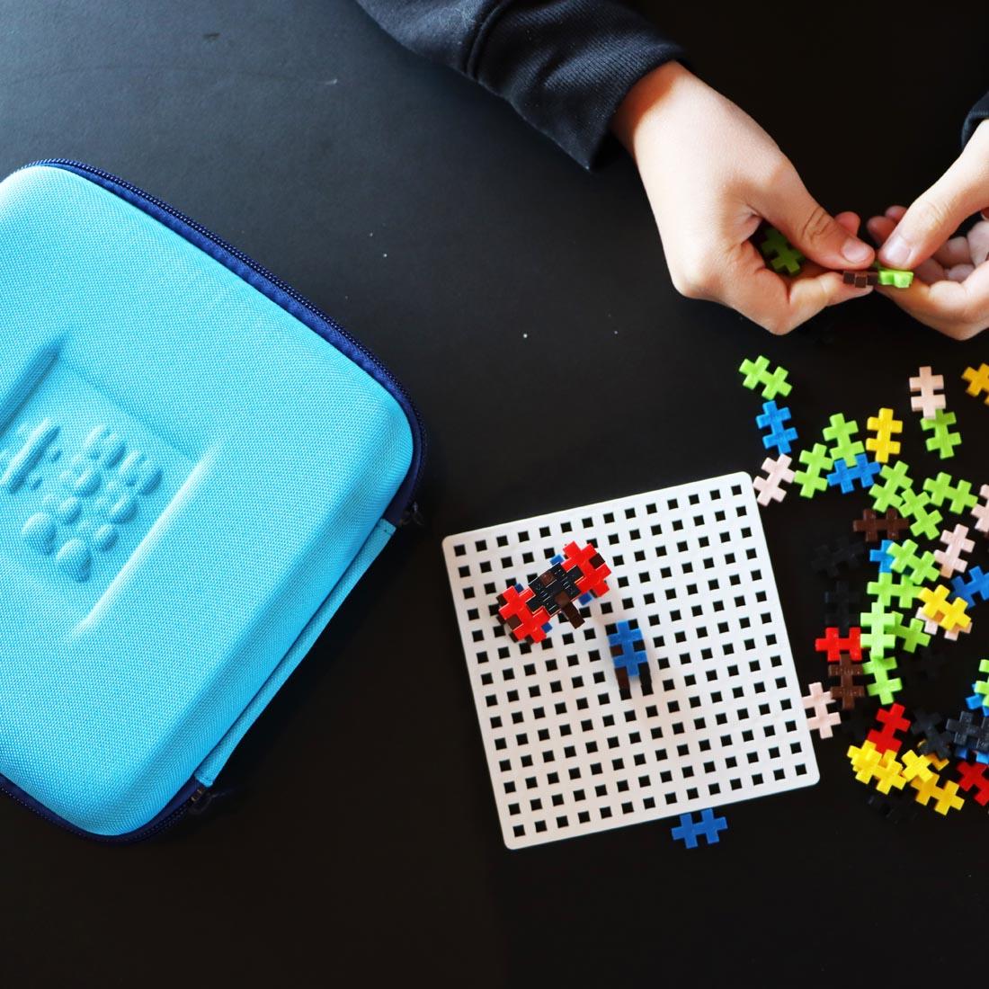 hands playing with Plus-Plus pieces beside the Plus-Plus Travel Case