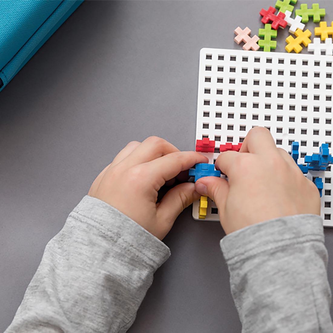 hands building with Plus-Plus pieces on a base plate