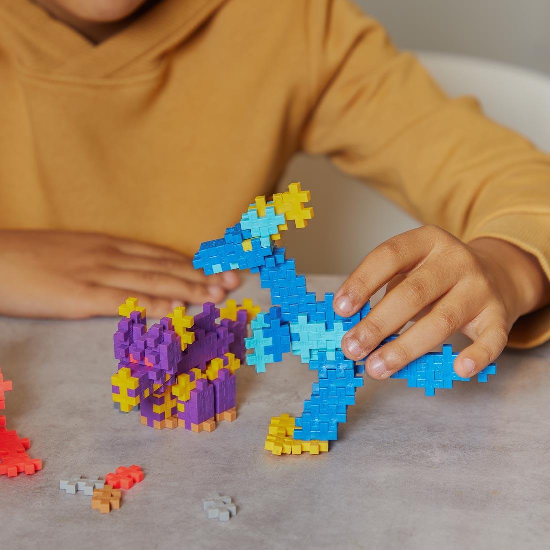 child's hands playing with creations made with the Plus-Plus Learn To Build Dinosaurs Set