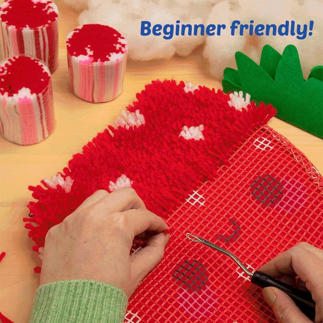 hands working on a Make A Strawberry Latch Hook Pillow by Craft-Tastic plus text Beginner friendly!
