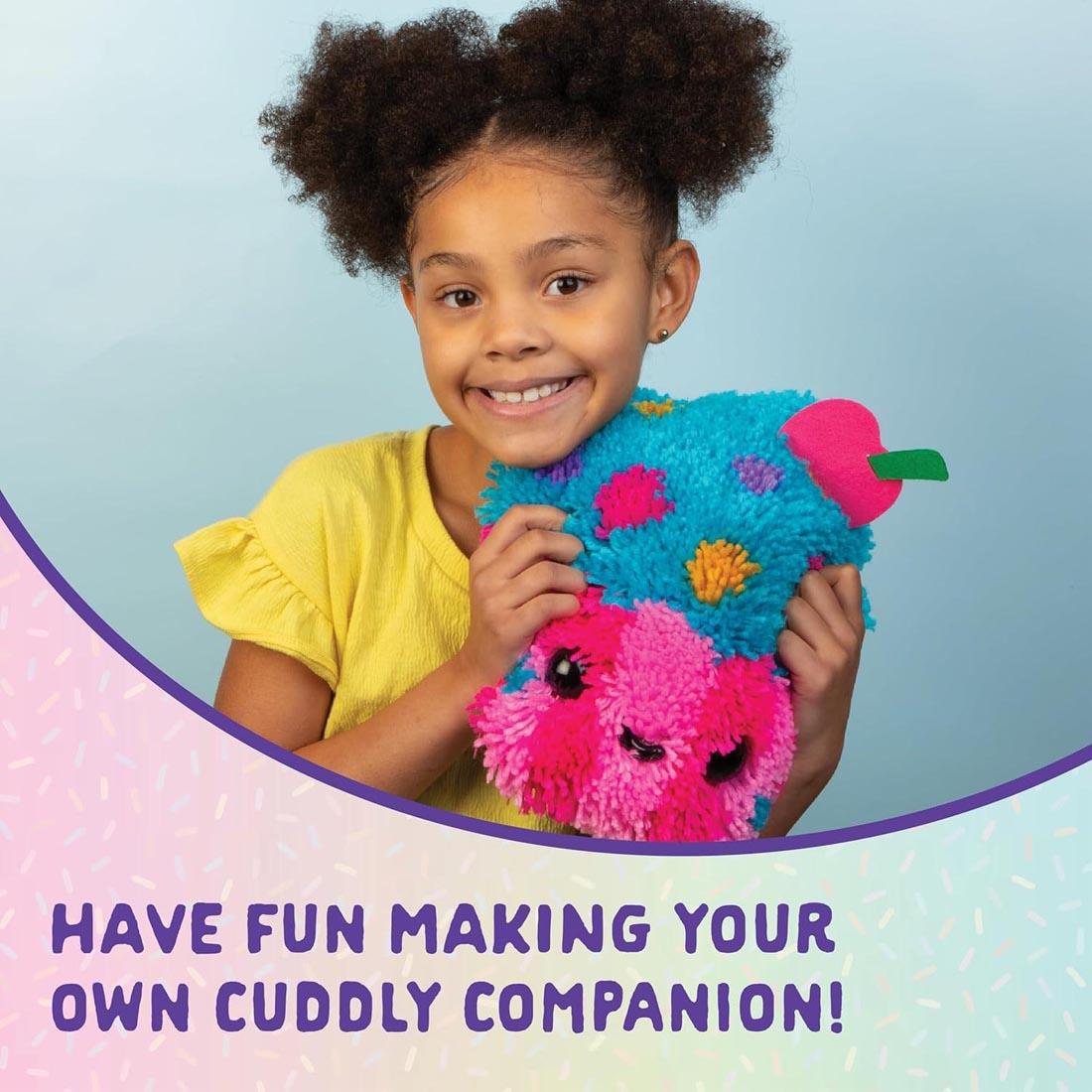 child hugging a completed Make A Cupcake Latch Hook Pillow by Craft-Tastic with text Have fun making your own cuddly companion!