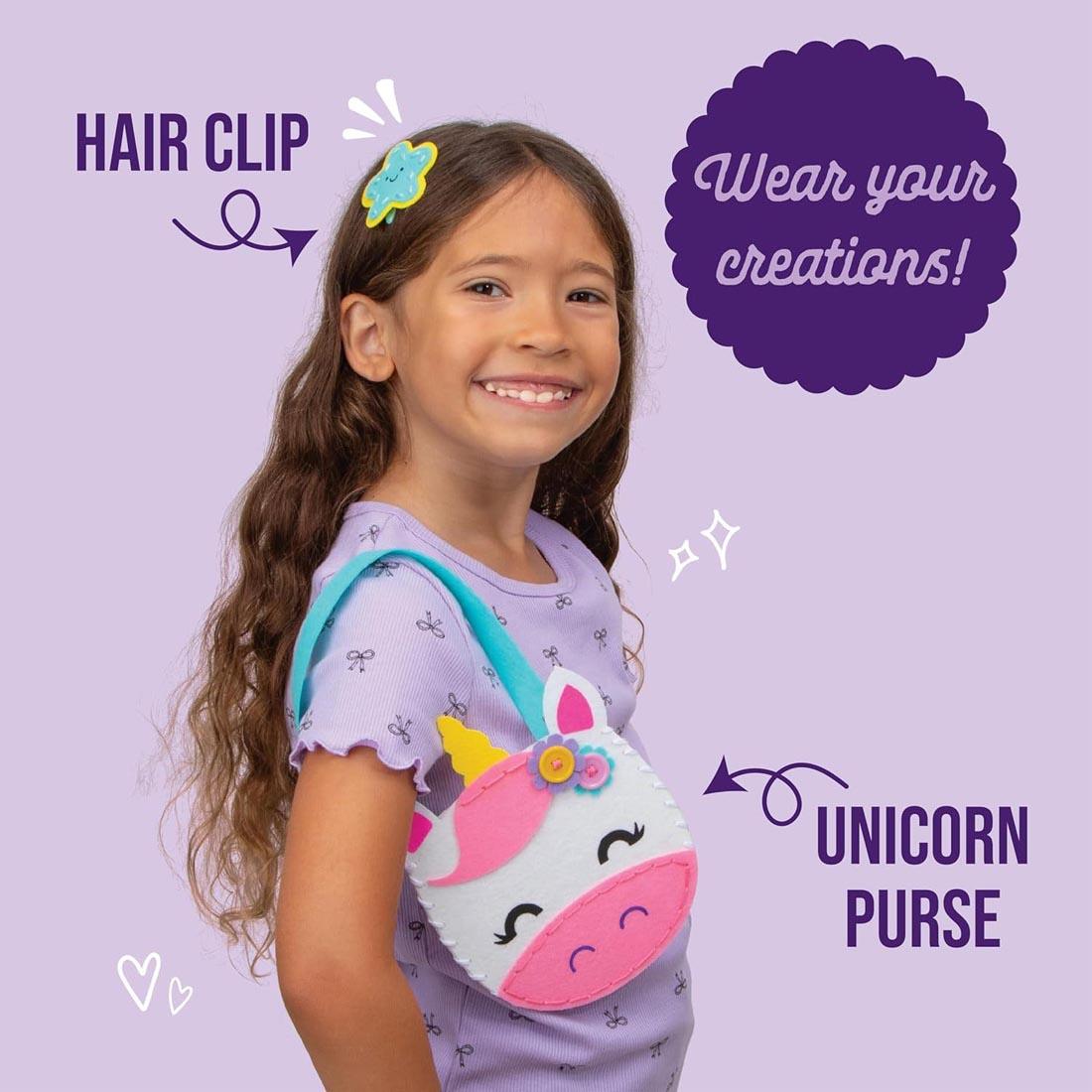 child wearing completed examples from Let's Learn Sewing Art Kit plus text Wear your creations! Hair Clip; Unicorn Purse