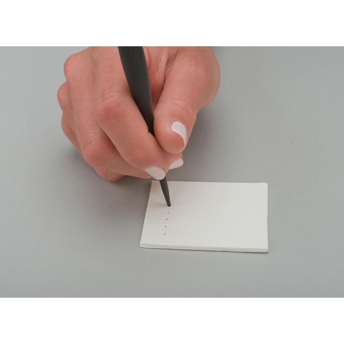Hand using plastic tool to make dots in a thin slab of clay