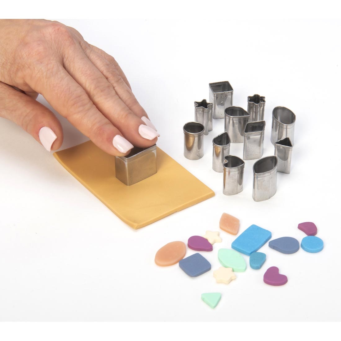 hand using a Mini Stainless Steel Cutter to cut out a shape from a thin slab of clay, plus other cutters and clay shapes on the side
