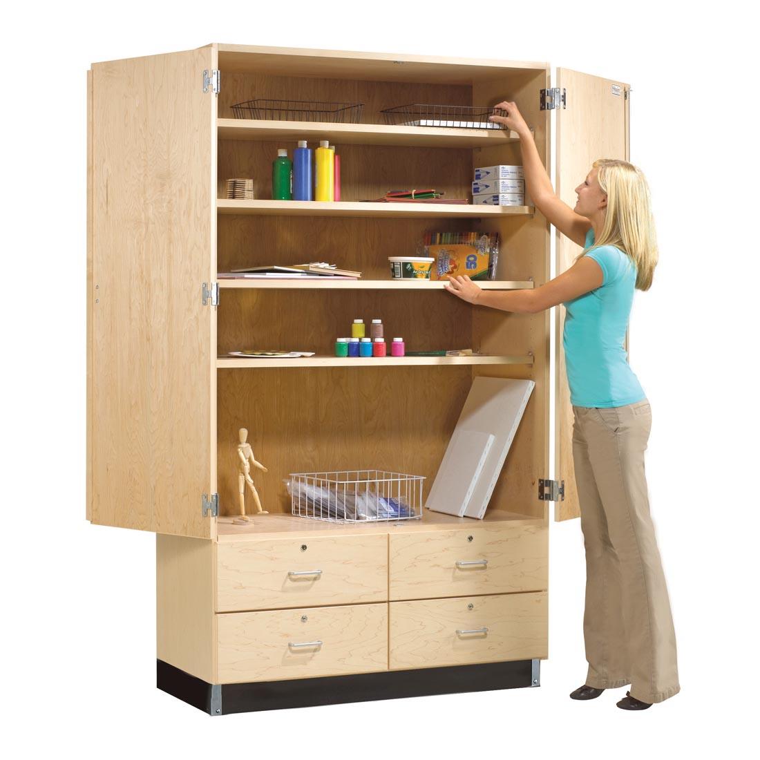 Adult reaching into General Storage Cabinet which is open and shown filled with art supplies