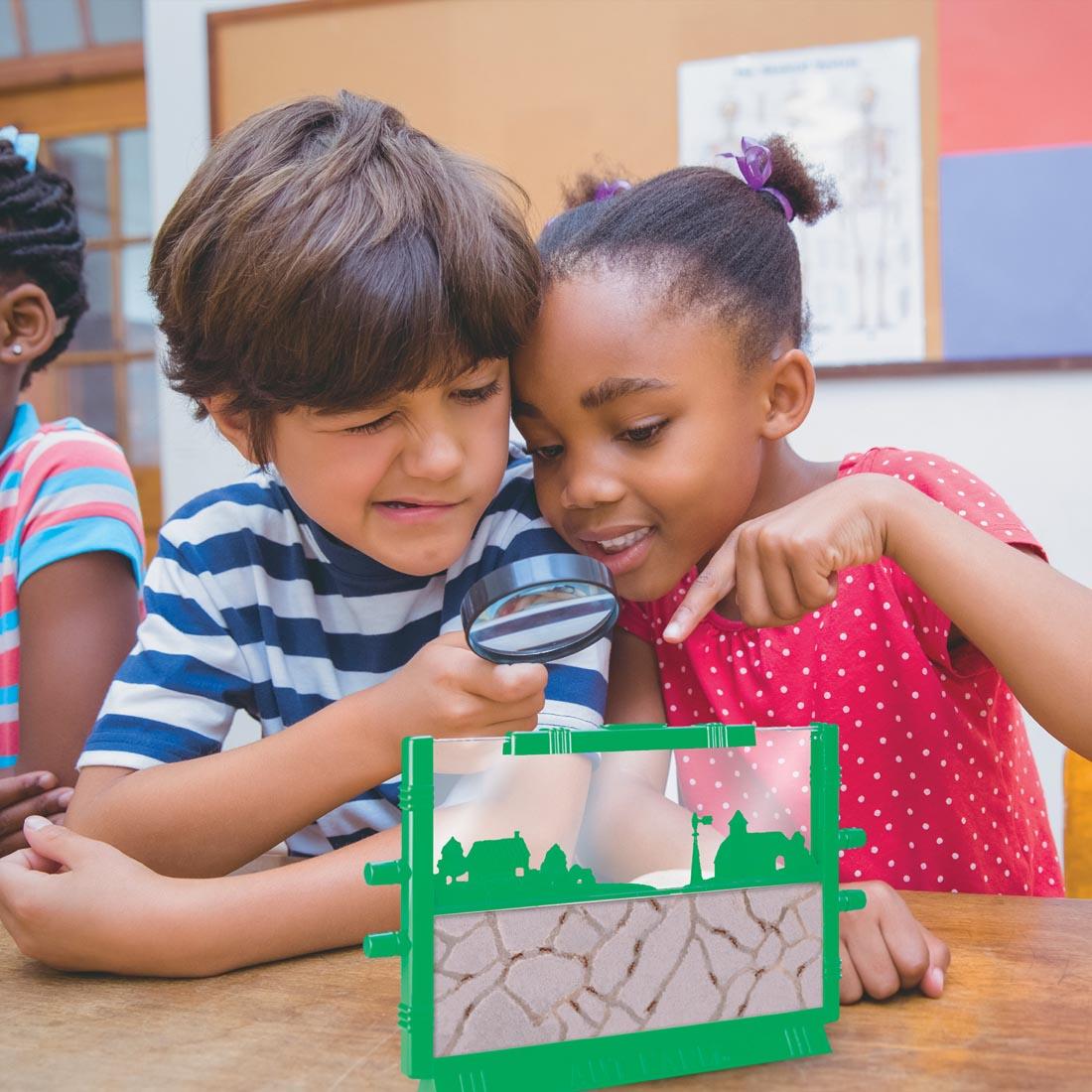 Children using a magnifying glass to peer into the Ant Farm