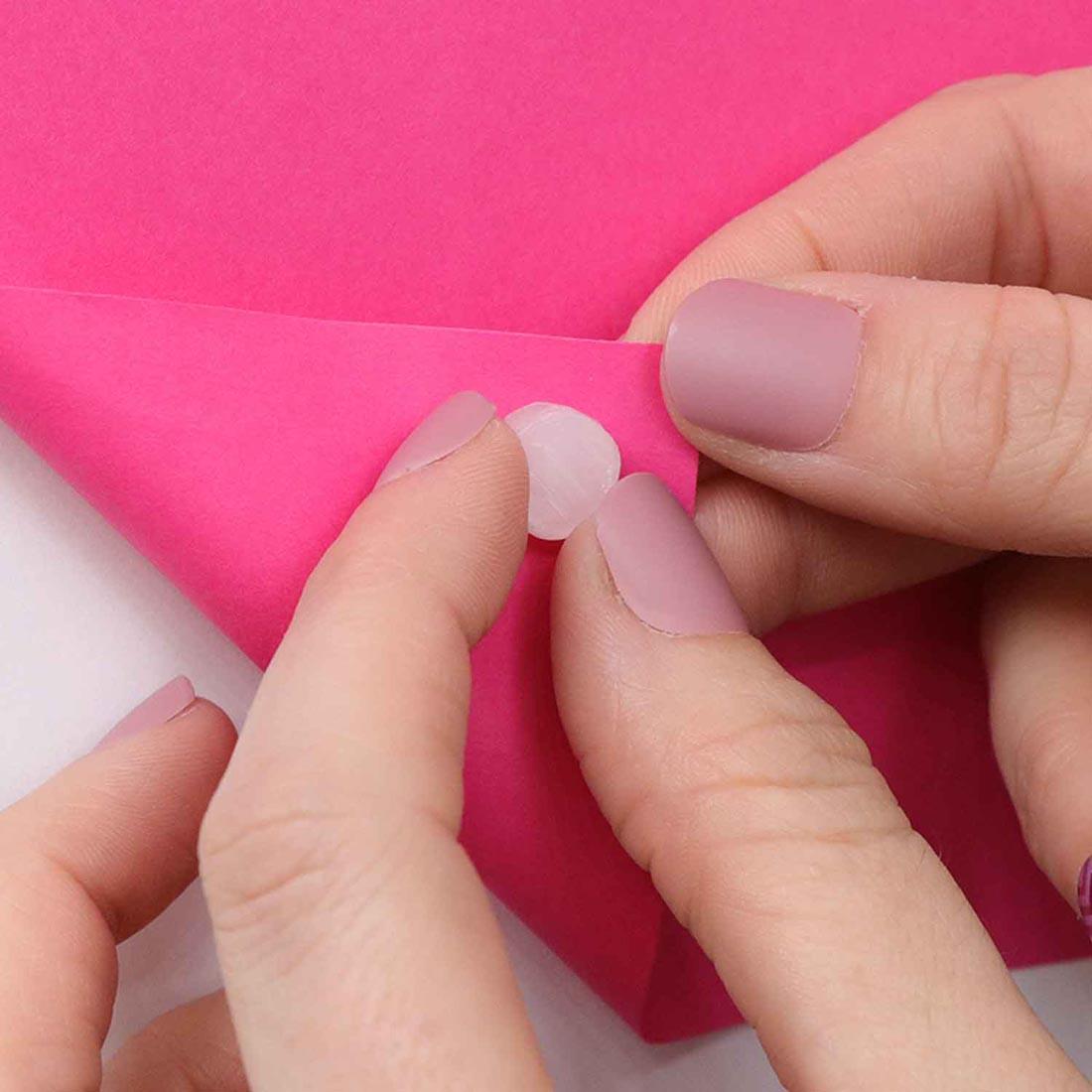 fingers attaching a StikkiDOT to the corner of a piece of bright pink paper