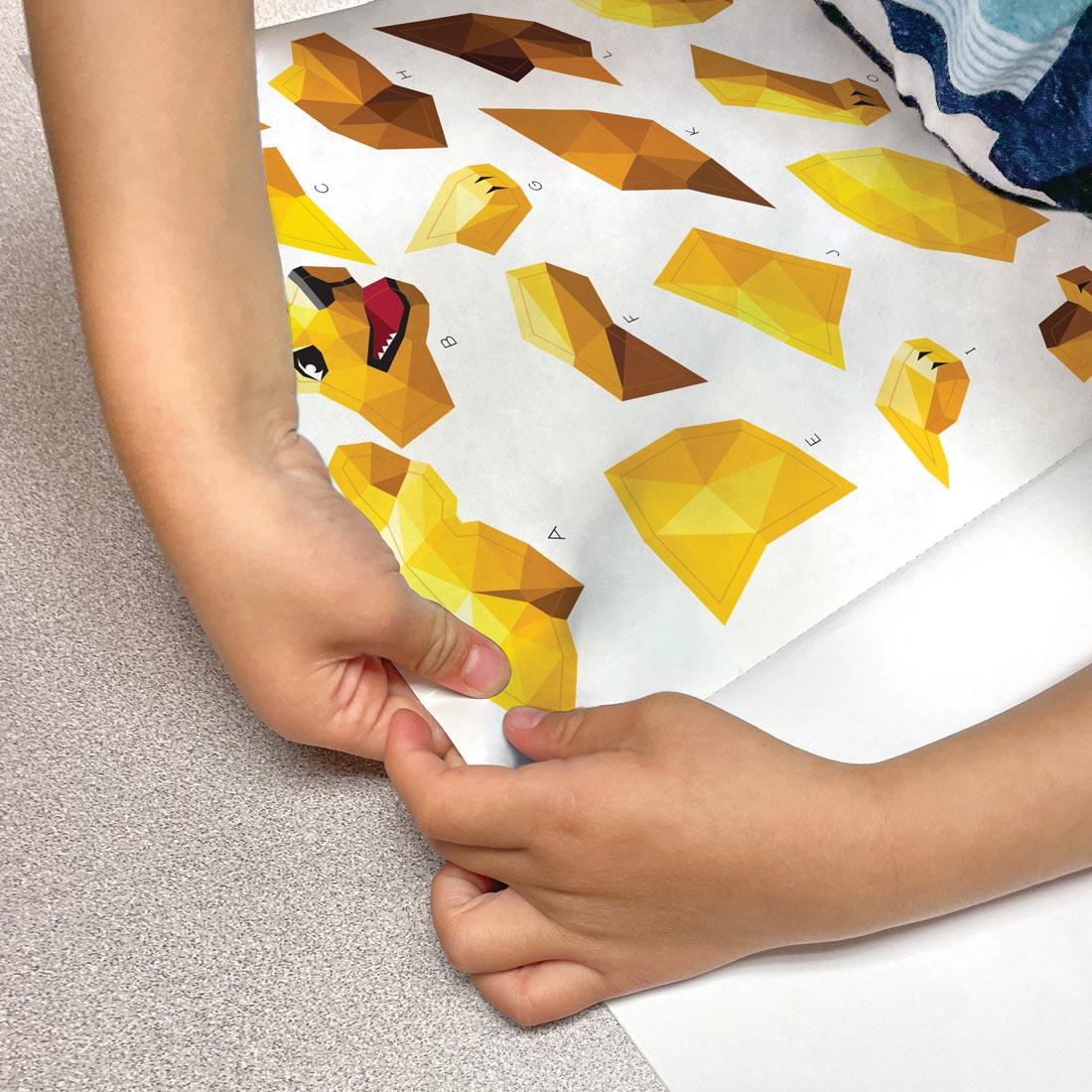 child's hands removing a sticker from a page of the Awesome Animals Modern Mosaics Stick To The Letters Book By Teacher Created Resources
