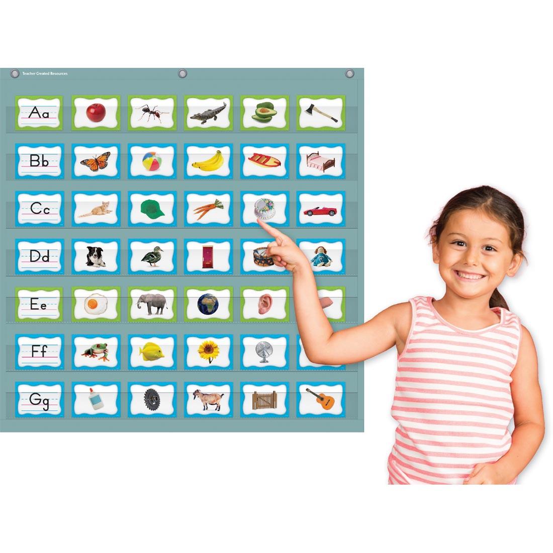 child pointing to the Calming Blue 7-Pocket Chart By Teacher Created Resources with cards in it