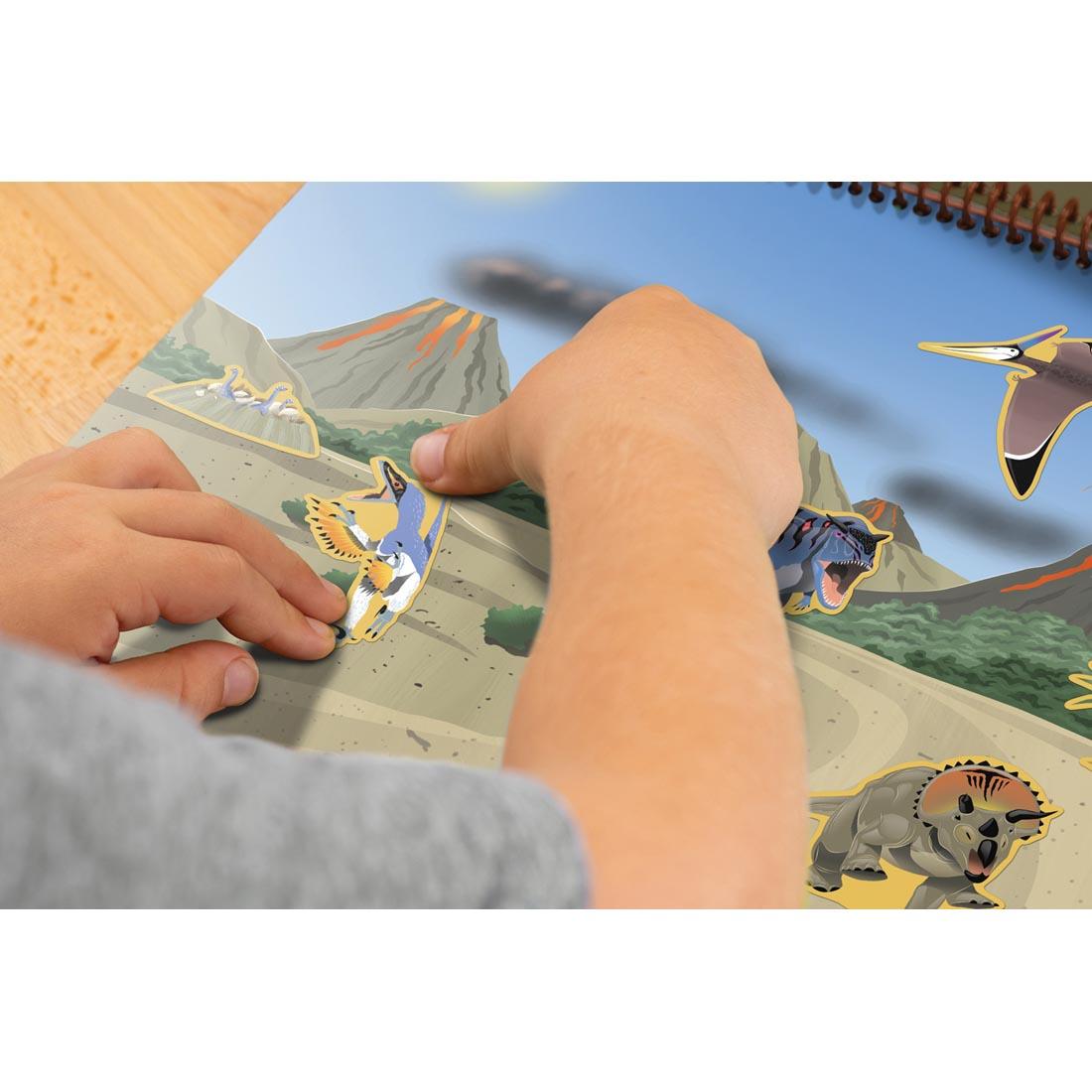 hands applying a sticker to the Dinosaurs And Prehistoric Animals Reusable Sticker Pad By Teacher Created Resources
