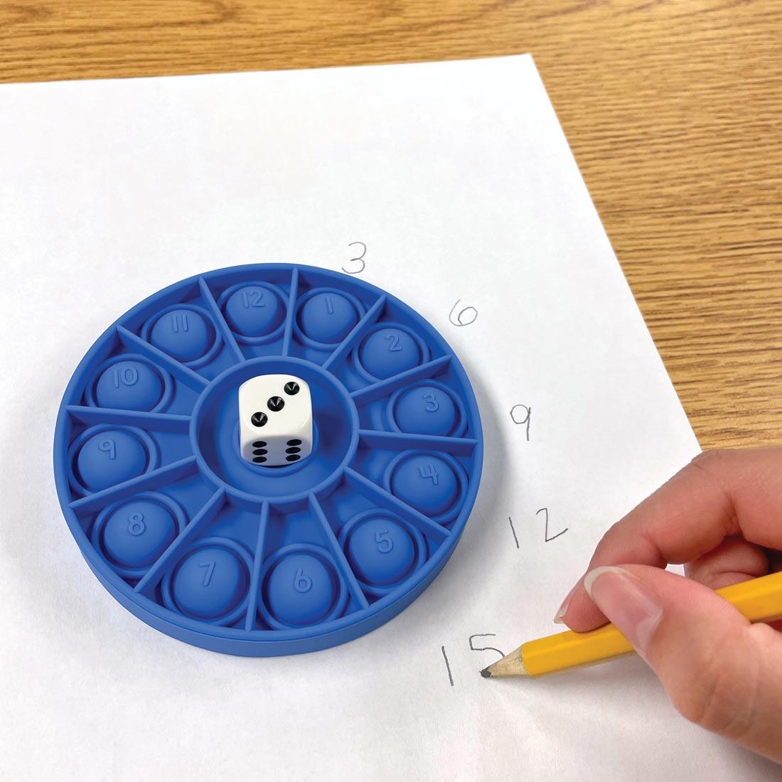 one of the Push And Pop Number Wheels with a die on top, sitting on paper with numbers being written on it