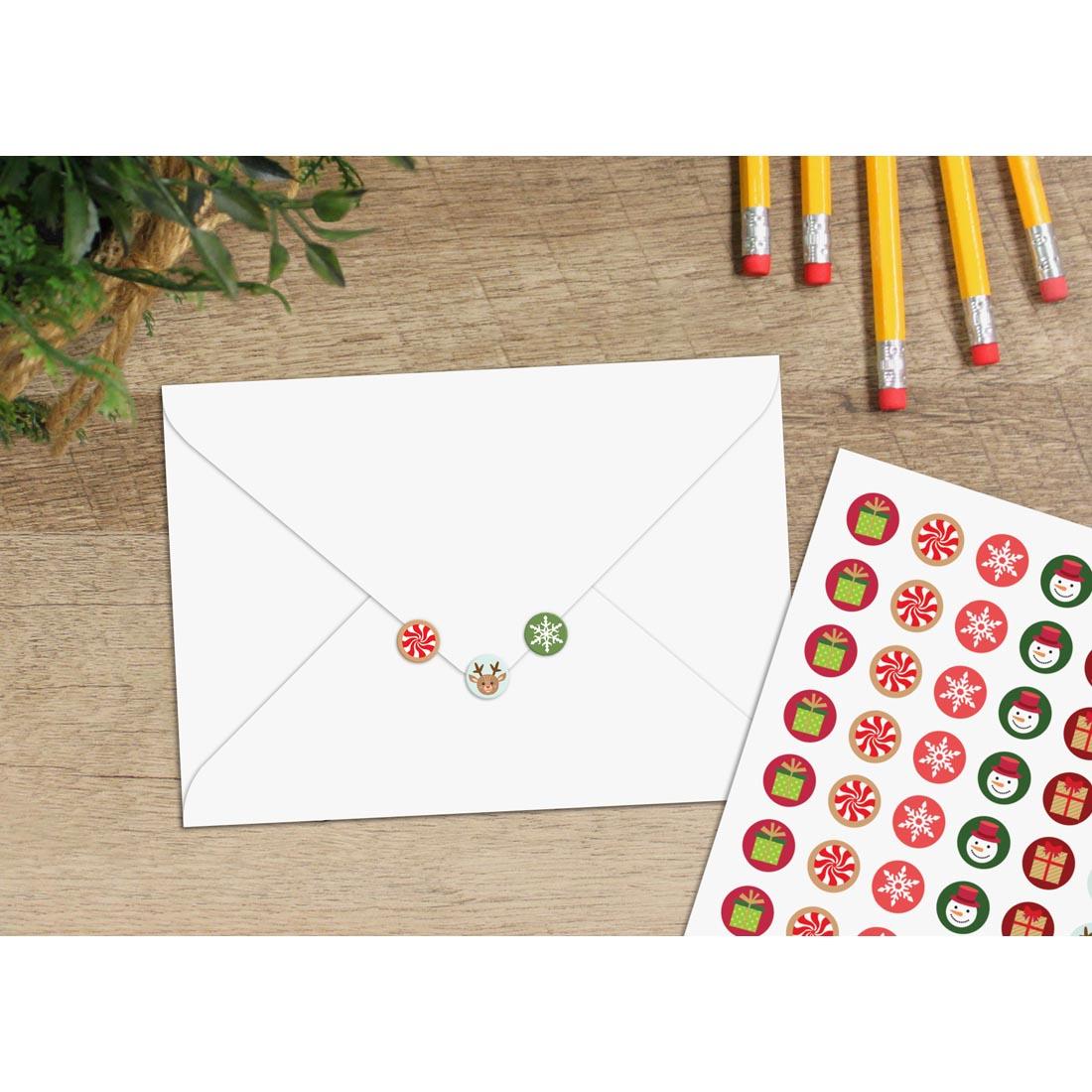 table with a sheet of Winter Holiday Mini Stickers and 3 stickers on a sealed envelope