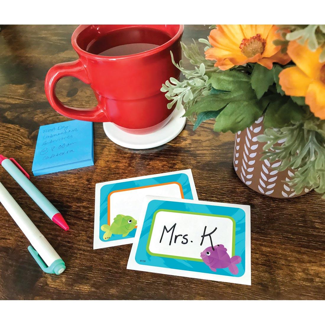 2 Colorful Fish Name Tags/Labels By Teacher Created Resources laying on a desk