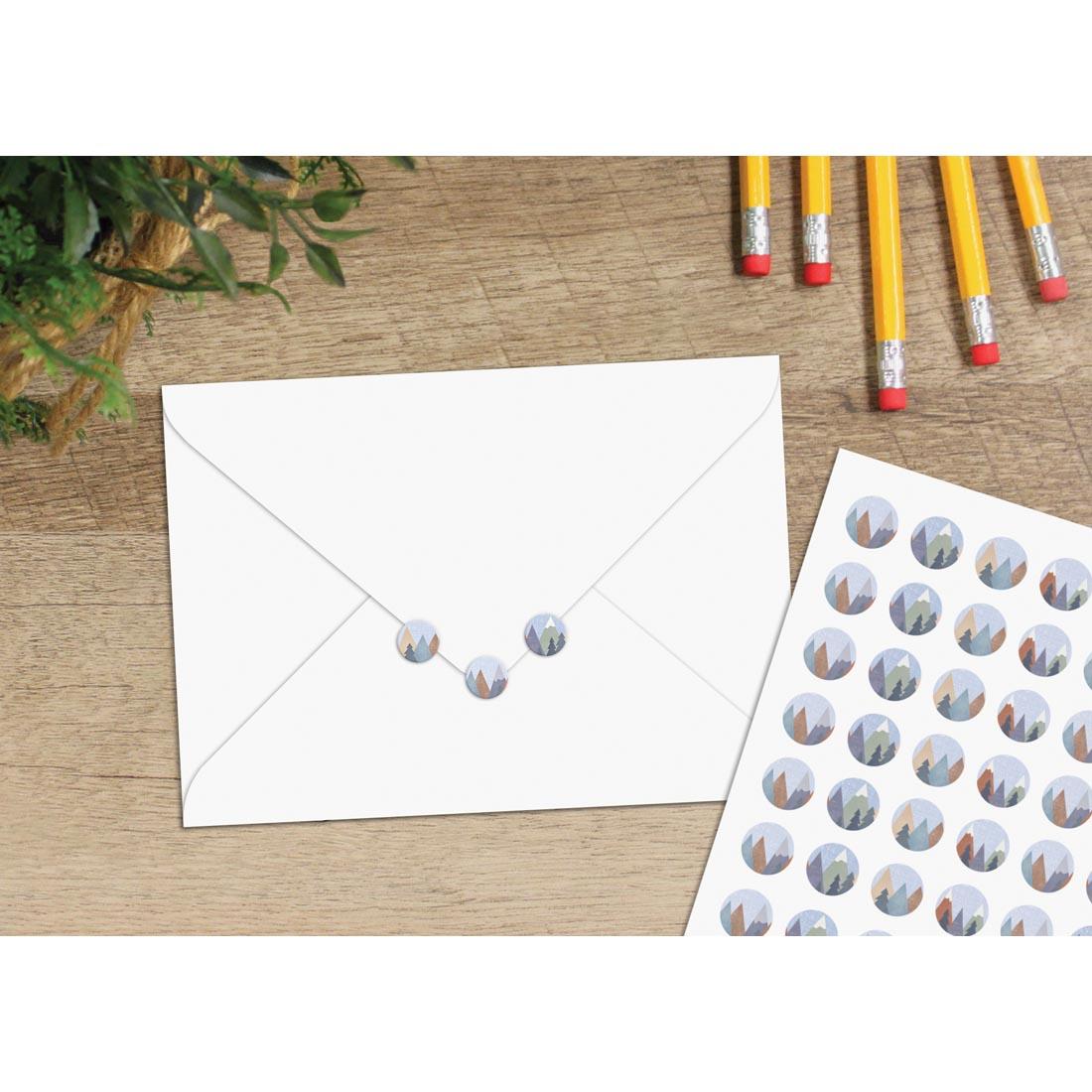 table with a sheet of Mini Stickers from the Moving Mountains collection by Teacher Created Resources plus 3 stickers on a sealed envelope