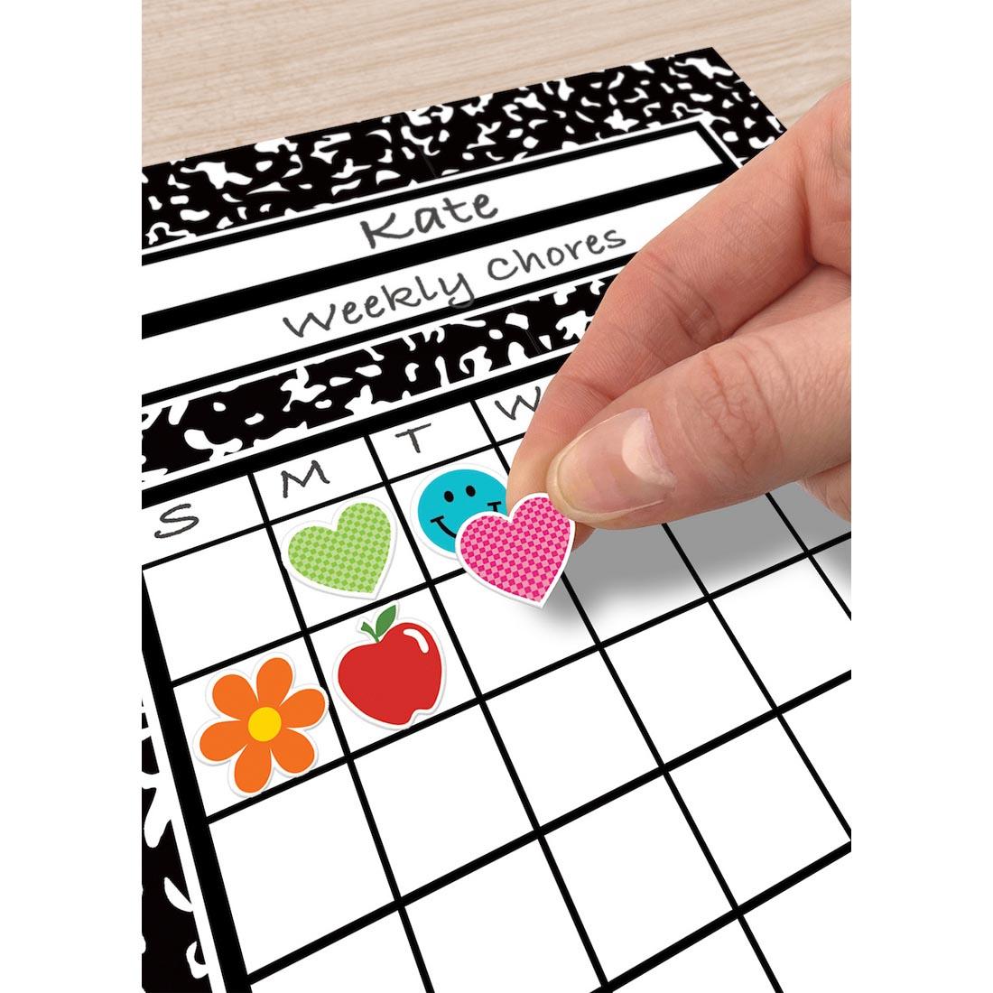 hand placing a Mini Sticker from the Cool For School collection by Teacher Created Resources onto an incentive chart