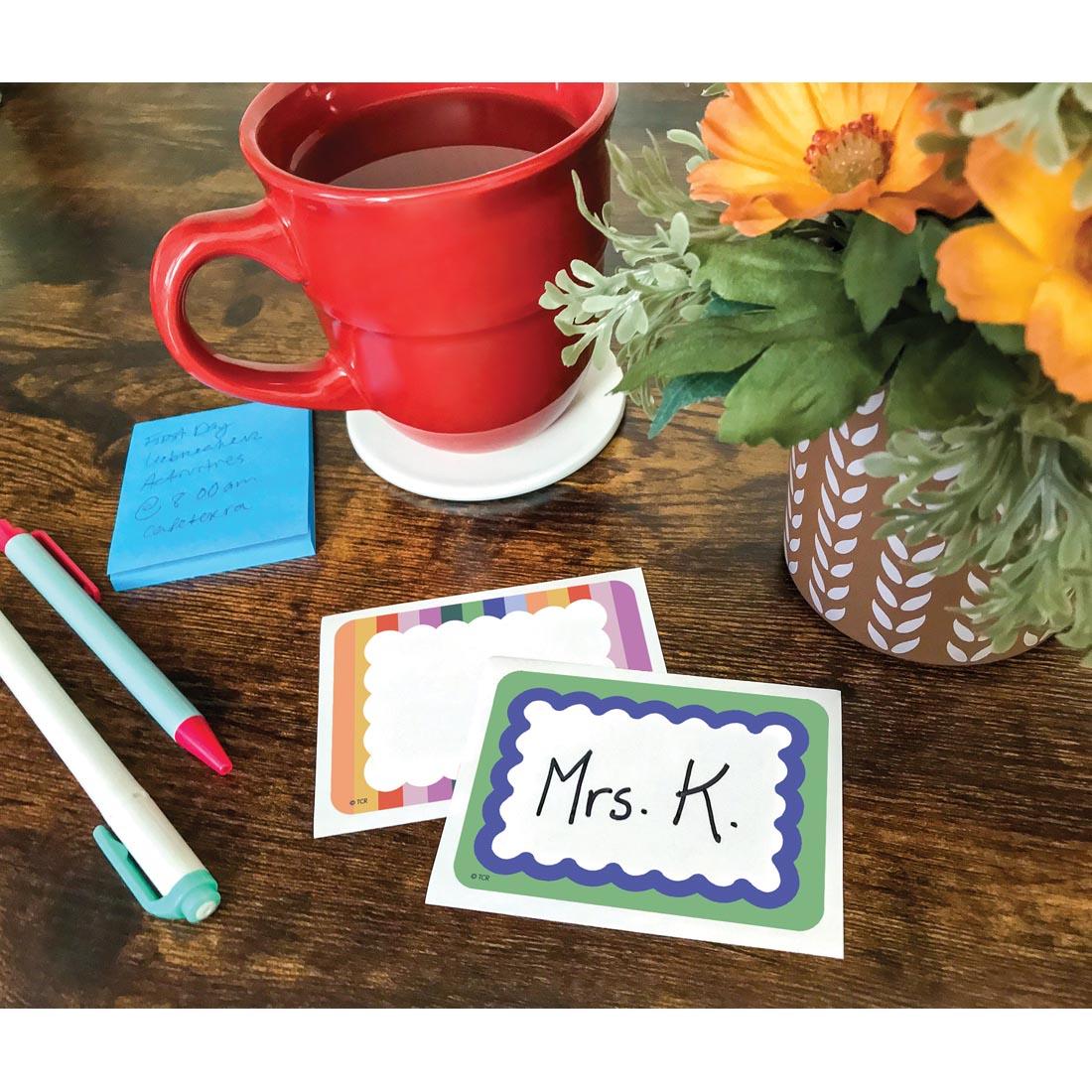 2 Name Tags/Labels from the Color Crush collection by Teacher Created Resources on a desk with pens, flower pot and coffee mug