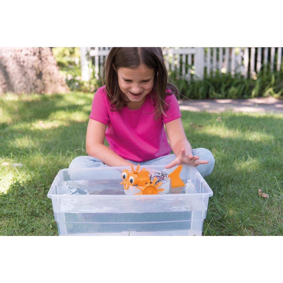 Child playing outside with the 4M Green Science Solar Hybrid Power Aqua Robot in a tub of water