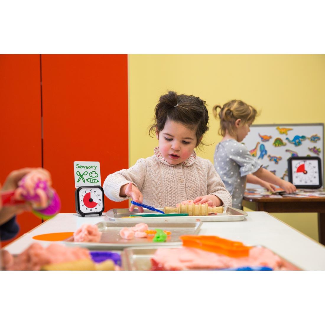 Child at a classroom table next to the Time Timer 3" 60-Minute Timer with the written note Sensory