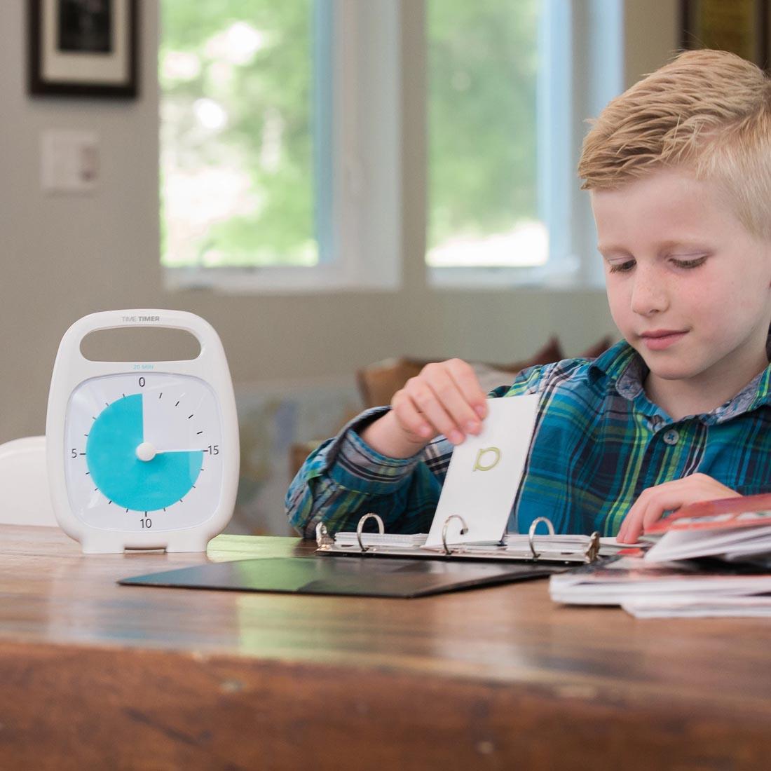 Child at a table with a flipbook next to the Time Timer PLUS 20-Minute Timer