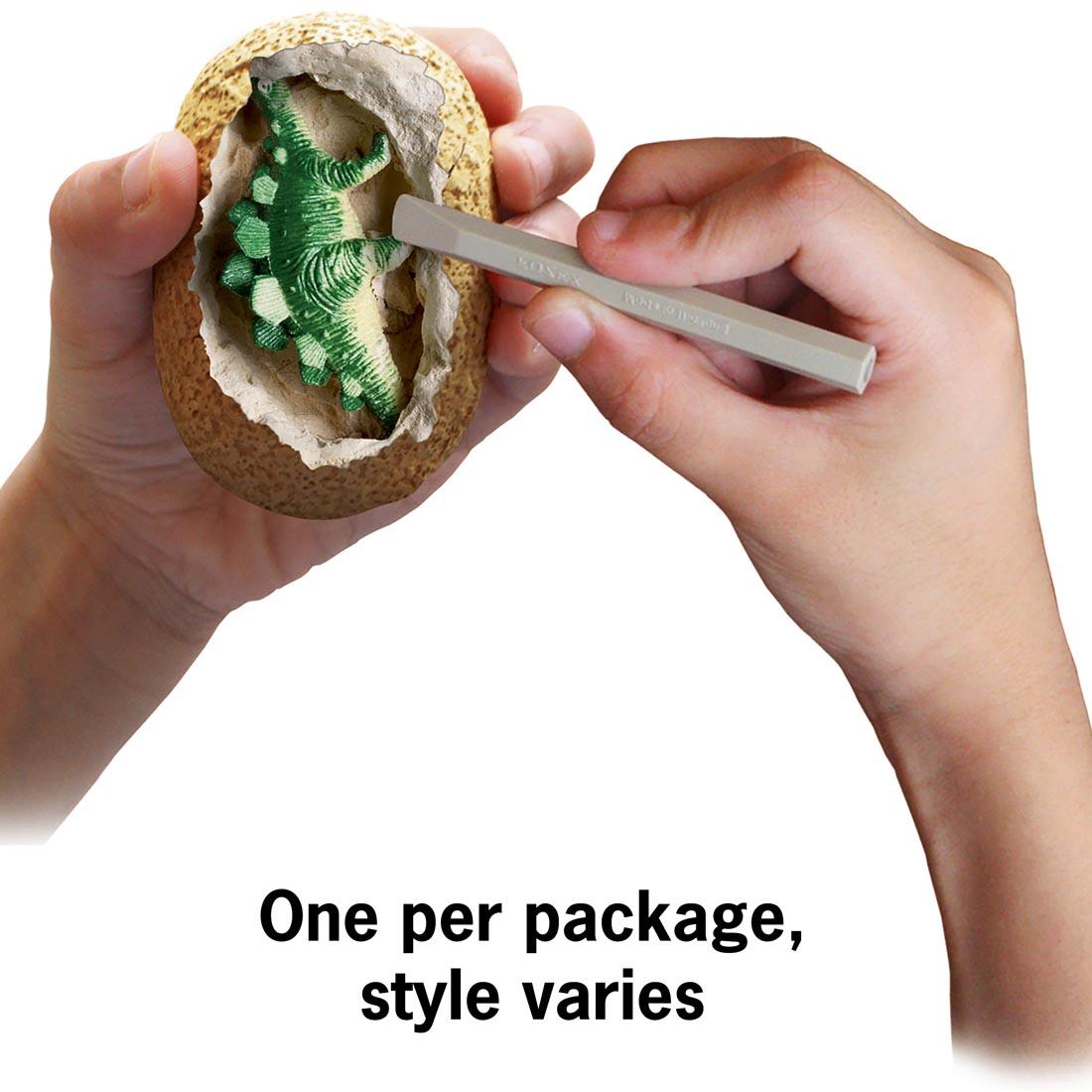 child's hands using the I Dig It! Dinosaur Egg Excavation Kit with text One per package; style varies