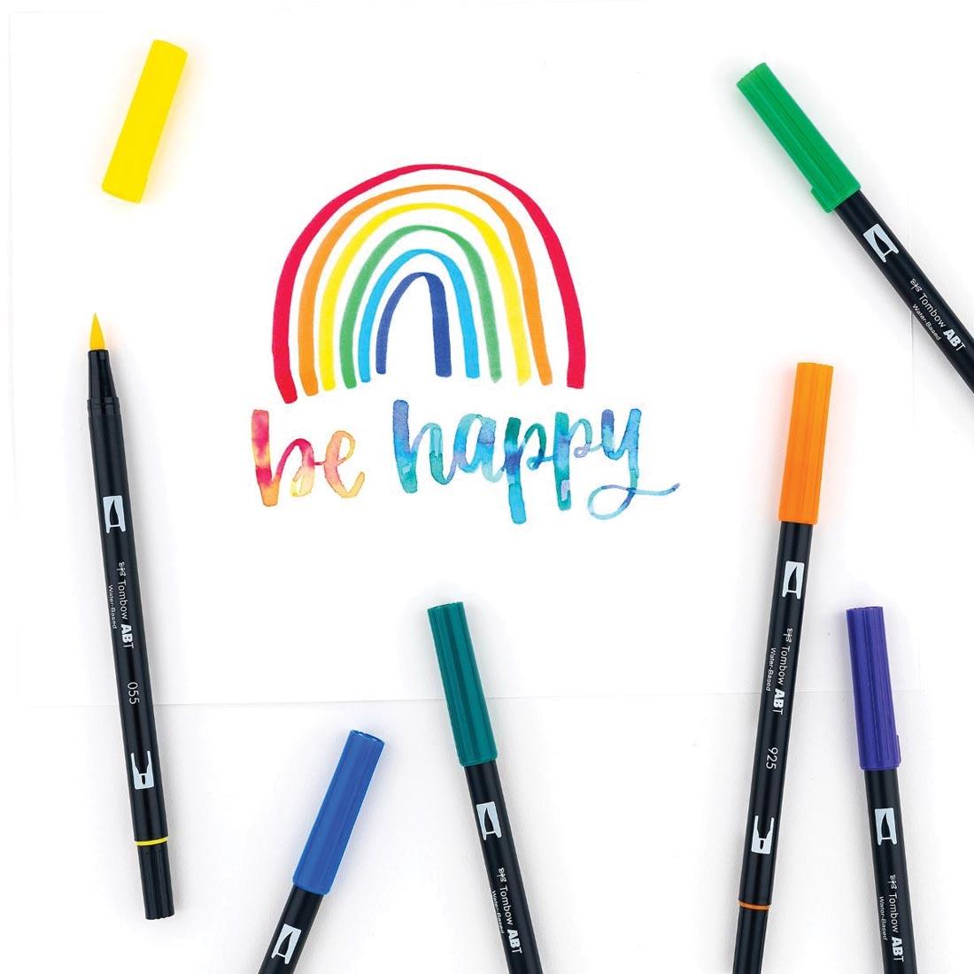 Several colors of Tombow Primary Dual Brush Pens on a drawing that says be happy