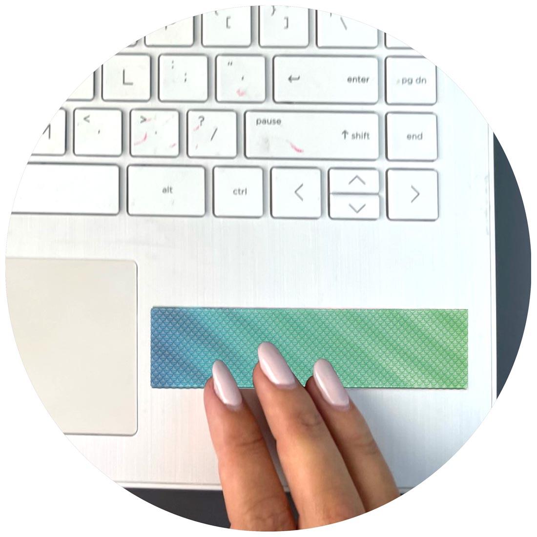 closeup of a laptop keyboard with a Bumpy Gradient Zen Strip attached to the corner and fingers rubbing it