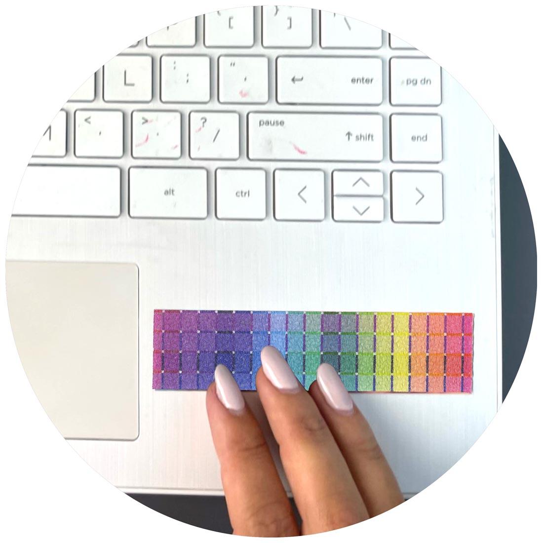 closeup of a laptop keyboard with a Sandy Brights Zen Strip attached to the corner and fingers rubbing it